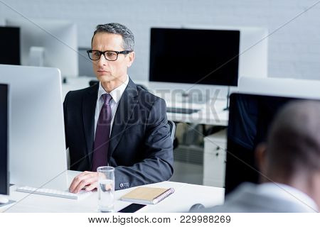 Selective Focus Of Focused Businessman In Eyeglasses Working On Computer In Office
