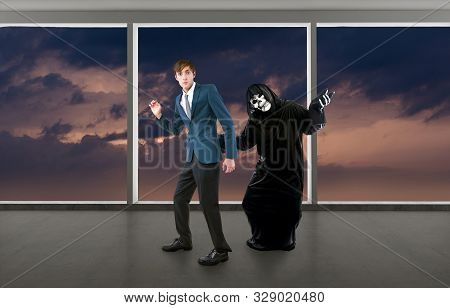 Man In A Halloween Grim Reaper Ghost Costume Chasing, Mocking And Making Fun Of Scared Businessman R