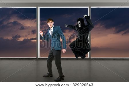 Man In A Halloween Grim Reaper Ghost Costume Chasing, Mocking And Making Fun Of Scared Businessman R