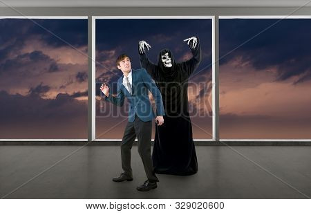 Man In A Halloween Grim Reaper Ghost Costume Chasing, Mocking And Making Fun Of Scared Businessman R