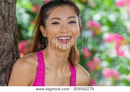 Outdoor portrait of a beautiful happy fit healthy young Chinese Asian young woman or girl laughing with perfect teeth wearing pink running vest with natural flower background