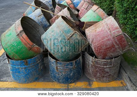 Row Of Old Dirty Used Oil Tanks Cut In Half And A Wooden Broom On Top