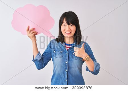 Young beautiful Chinese woman holding cloud speech bubble over isolated white background happy with big smile doing ok sign, thumb up with fingers, excellent sign