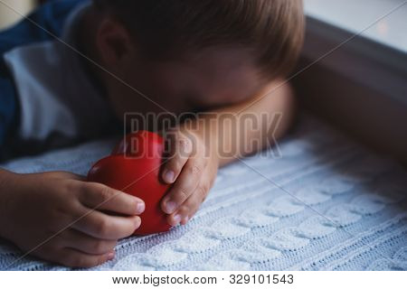 Sad And Desperate Child Boy Holding Red Toy Heart In Hands And Hiding His Face. Copy Space. Concept 