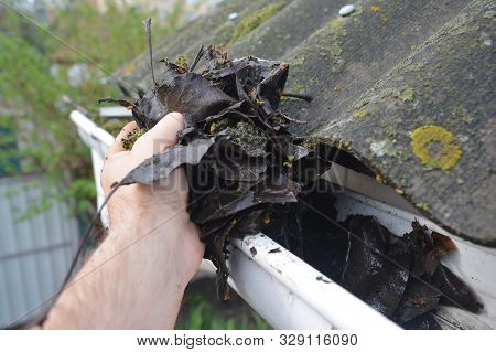 Roofer Cleaning Rain Gutter From Leaves In Spring. Roof Gutter Cleaning Tips. Clean Your Gutters Bef