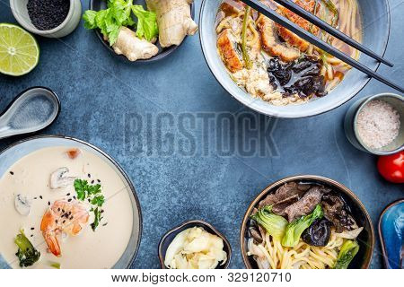 Set Of Serving Asian Soups On Dark Blue Background Top View. Tom Yum Soup, Eel Fish Soup And Ramen N