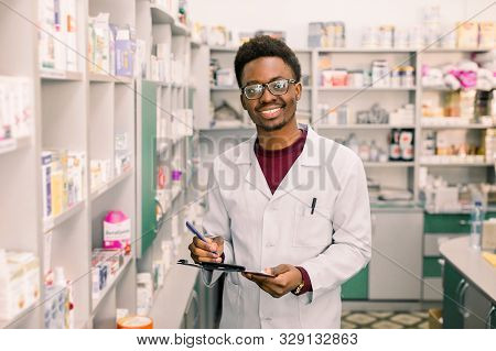 Smiling African American Man Pharmacist Or Chemist Writing On Clipboard While Standing In Interior O