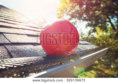 Red soccer ball stuck on gutter mesh on a roof