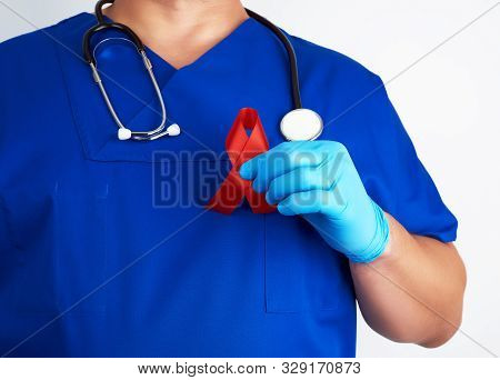 Doctor In Blue Uniform And Sterile Latex Gloves Holds A Red Ribbon - A Symbol Of The Fight Against D
