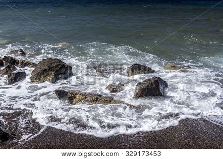 Sea Surf On The Beach With Black Volkanic Sand And Stones.