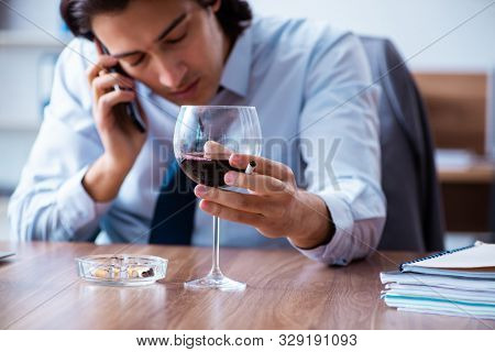 Male employee drinking alcohol and smoking cigarettes at workpla