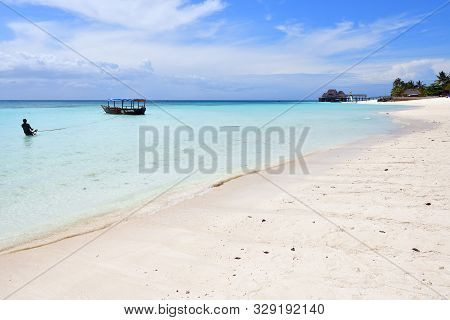Kendwa, Tanzania - October 3, 2019: White Sandy Beach And Local Man Tows A Wooden Boat In Clear Wate