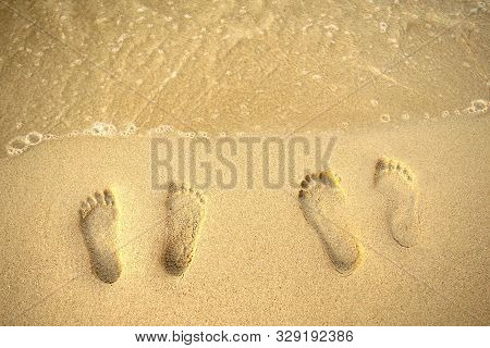 Feet Prints On The Sand Of The Beach And Sea Wave. Top View. Two People Foot Marks On Sand.