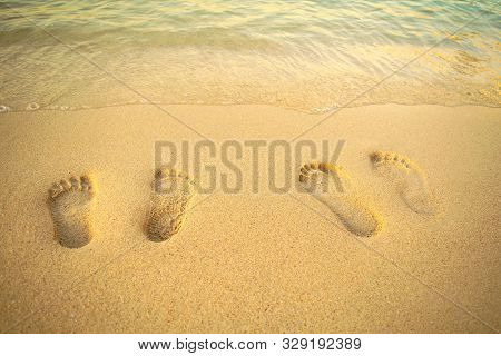 Feet Prints On The Sand Of The Beach With Sea Wave. Top View. Two People Foot Marks On Sand.