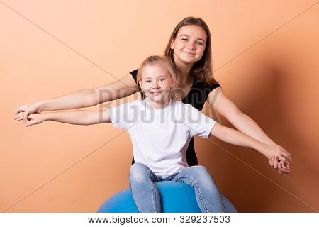 Girls On A Gymnastic Ball, On A Light Orange Background.