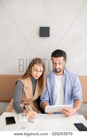 Two young clever students sitting by table in cafe and workng over project or presentation before seminar or conference