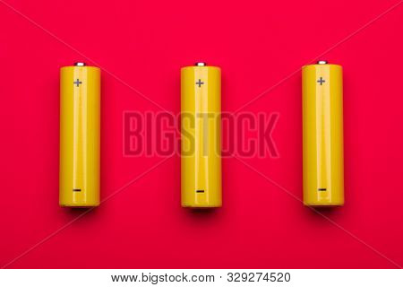 Top view of 3 yellow AA alkaline or rechargeable NiMH batteries on red background
