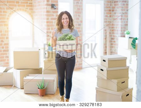 Middle age senior woman moving to a new house packing cardboard boxes happy with big smile doing ok sign, thumb up with fingers, excellent sign
