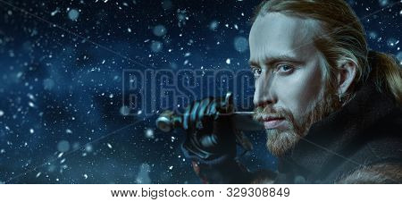 Close-up portrait of a medieval knight in armour and with a sword over winter background. Historical reenactment. Copy space.