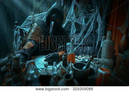 The plague doctor is working at his desk, inventing a cure for bubonic plague. The atmosphere of mysticism. Historical reenactment. Halloween. 