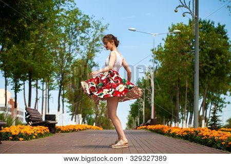 Full body portrait of a beautiful young brunette woman walking in flowers dress, summer park outdoors