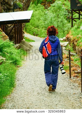 Tourist Woman With Norwegian Flag And Camera Walking Trough Mountains Path In Allmannajuvet Area Sau