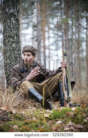 A Soldier Of World War Ii With A Rifle Is Sitting By The Tree And Smoking