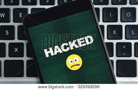 Sim-swap Attack Concept. Smartphone With Hacked Inscription And Sad Emoji Icon On Screen Over Laptop