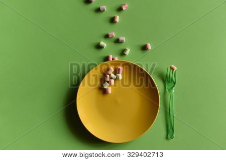 An Empty Yellow Plate On A Green Background. There Is A Marshmallow On The Green Fork. Multicolored 