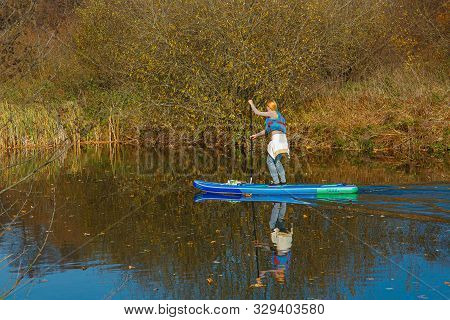 Girl Swims On A Sup Board On The River. Around The Autumn Forest.