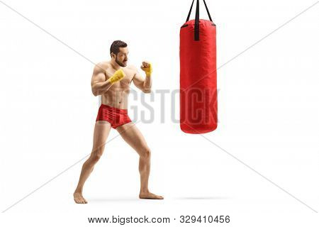 Full length shot of a muscular young man exercising kickboxing with a punching bag isolated on white background