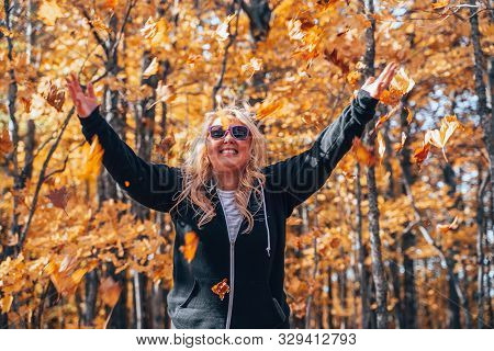 Cute Woman Throwing Leaves In The Autumn Forest, Wide Angle View On A Sunny Fall Day