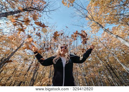 Cute Woman Throwing Leaves In The Autumn Forest, Wide Angle View On A Sunny Fall Day