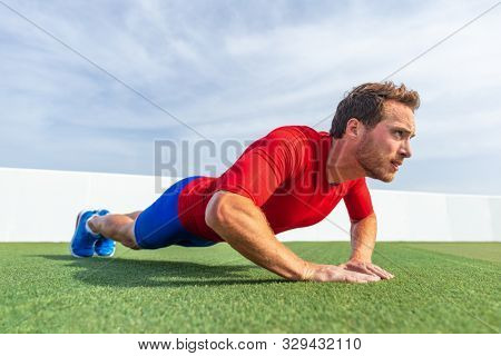 Fitness man doing diamond hand push ups exercises at outdoor grass park. Core body workout athlete planking or doing pushup.