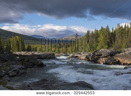 Beautiful Northern Landscape With Wild Glacier River Kamajokk, Boulders And Spruce Tree Forest In Kv