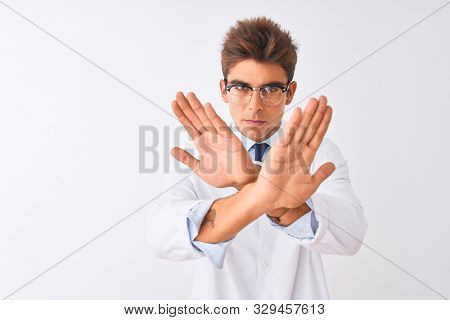 Young handsome sciencist man wearing glasses and coat over isolated white background Rejection expression crossing arms and palms doing negative sign, angry face