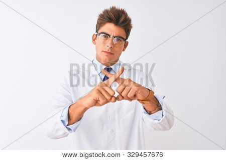 Young handsome sciencist man wearing glasses and coat over isolated white background Rejection expression crossing fingers doing negative sign