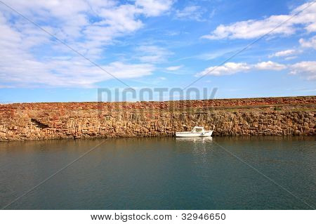 Old, fishing harbour in Dunbar with stone wall and a small white boat