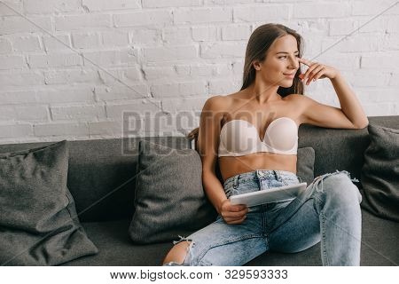 Beautiful Happy Woman In White Bra And Jeans Using Digital Tablet On Sofa