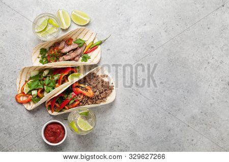 Set of mexican tacos with meat and vegetables in tortilla. And caipirinha cocktail. Top view on stone table. Flat lay with copy space