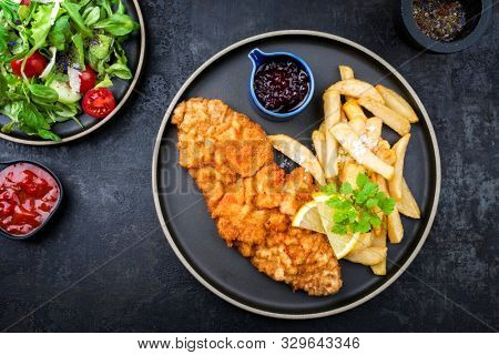 Fried Wiener schnitzel from veal topside with French fries and lettuce as top view on a modern design plate 