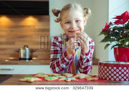 Portrait Of Pretty Little Girl With  Funny Pigtails Decoraiting Christmas Cookies