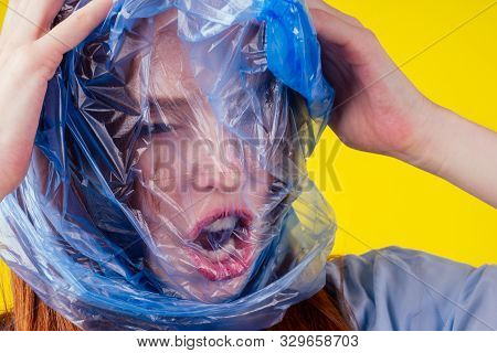 Redhaired Ginger European Woman Suffocation Head In Blue Polyethylene Package In Studio Yellow Backg