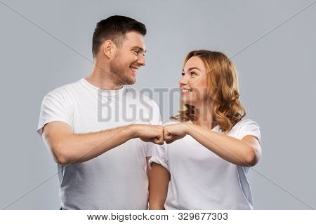relationships, friendship and people concept - portrait of happy couple in white t-shirts making fist bump gesture over grey background