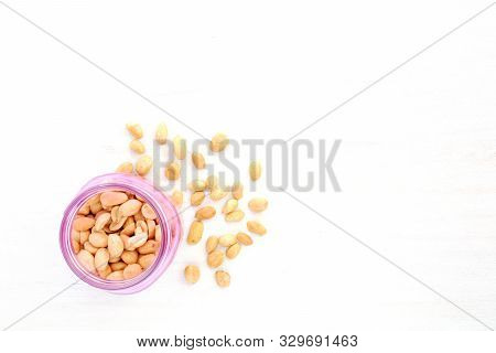 Roasted Organic Unsalted Peanuts Spilling From Pink Jar On Rustic White Wood Background. Shot From O