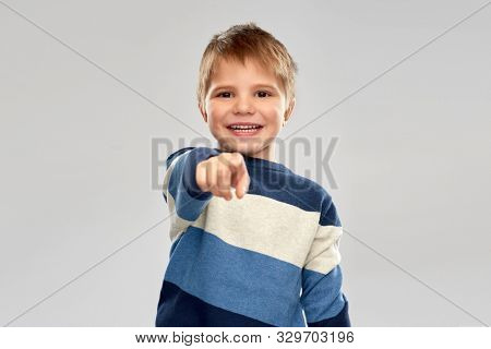 childhood, gesture and people concept - portrait of smiling little boy in striped pullover pointing finger over grey background