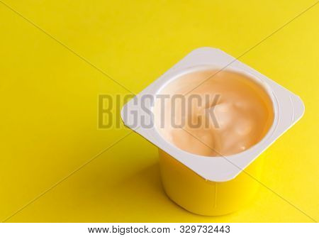 Peach Flavoured Yogurt In Yellow Plastic Cup Isolated On Bright Yellow Background With Space For Tex