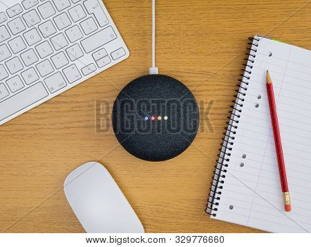 Smart Home Speaker Device Lit Up On Wooden Desk Table With Notepad Keyboard And Mouse