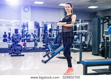 Young Beautiful Sportswoman With Nice Body. Brunette Fitness Girl Stands With Crossed Hands. Gym Bac