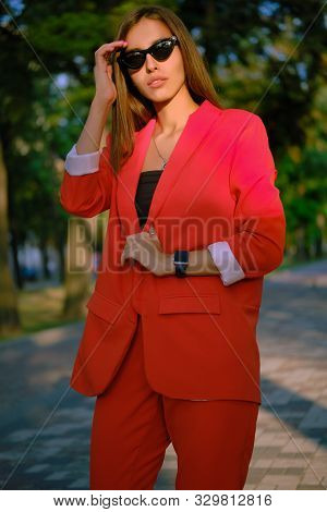 Blonde Girl In A Red Lady-type Pantsuit And Black Top, Watch, Ring, Pendant And Sunglasses Is Walkin